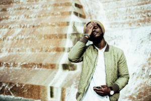 A young black man places a hand on his face as he receives disappointing news from his cell phone.