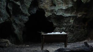 A manger filled with hay and swaddling cloths sits in a cave.