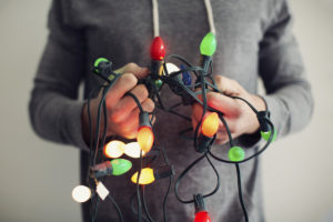 A man clutches a string of tangled Christmas lights.