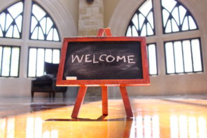 A small chalkboard with the word "Welcome" sits inside a large gothic room.
